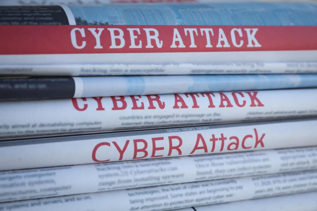 Stacked newspapers with headlines CYBER ATTACK as background.