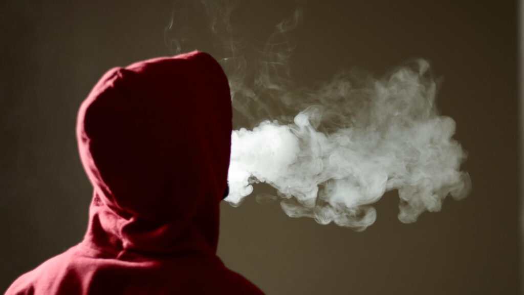 Teen in hoodie exhaling cloud of vapor