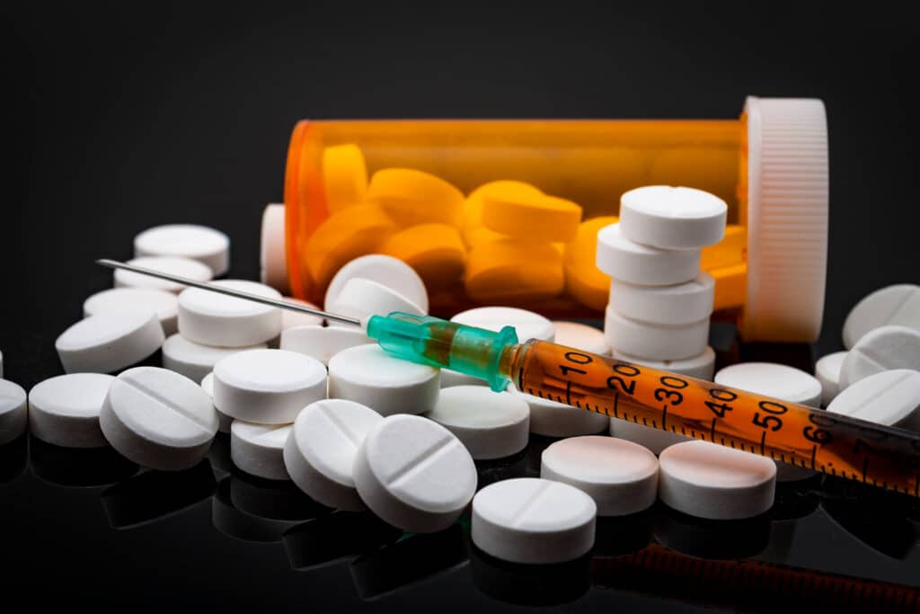 syringe on top of opioid pills next to medication bottle